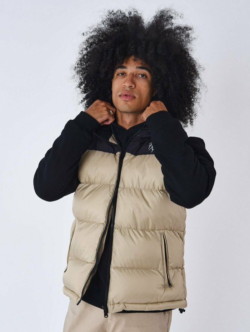 Gilet imbottito beige e nero, con chiusura zip frontale, tasche laterali e texture trapuntata. Il design include un colletto nero.