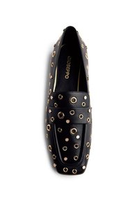 Mocasines de cuero negro adornados con ojales de metal en tono dorado, con punta cuadrada y suela plana. Nombre de la marca visible en el interior.
