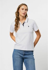 Witte poloshirt met een navy kraag en een knoopsluiting met drie knopen, voorzien van een klein geborduurd logo op de linkerborst en een ontspannen pasvorm.