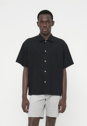 Camicia nera a maniche corte con bottoni bianchi e colletto, caratterizzata da una vestibilità comoda, abbinata a pantaloncini di colore grigio chiaro con trama.