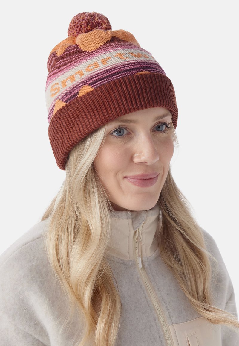 Knit beanie in orange, cream, and burgundy with a pom-pom on top. Features striped pattern and "Smartwool" text in bold letters. Ribbed edge.