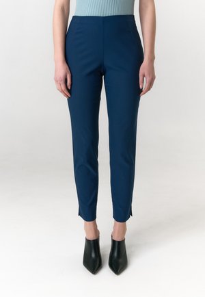 Marineblauwe taps toelopende broek met een gladde textuur en zijslitsen aan de zoom, gecombineerd met zwarte puntige enkellaarzen.