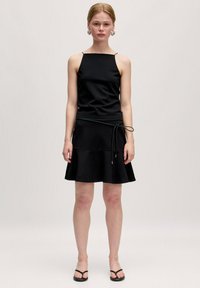 Schwarzes ärmelloses Kleid mit eng anliegendem Oberteil und schwingendem Rock, mit einem Kordelzug in der Taille. Glatte Textur, minimalistisches Design.