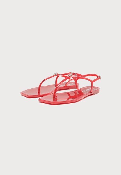 Sandales plates rouges brillantes avec fines brides et design à lanière entre les orteils, avec de petites décorations métalliques près de la boucle de la cheville.