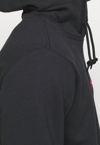 Svart hoodie gjort av mjukt material med en känguruficka, justerbar dragsko i huvan och subtil logotypdetalj. Har ribbade muddärmar.