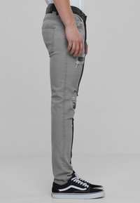 Grå skinny jeans med slitte detaljer, svarte side-striper, og en blå denim tekstur. Kombinert med svarte joggesko med hvite detaljer.