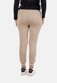 Joggers beige a maglia con caviglie affusolate e cintura elastica, abbinati a sneakers bianche con marchio nero sul tallone.