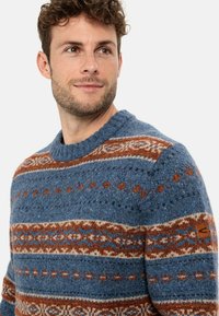Knitted blue sweater featuring brown and cream patterned stripes, round neck, and a brand patch on the left sleeve. Textured yarn.