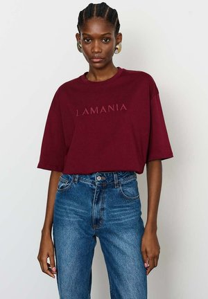 Burgundi trumpas rankovės marškinėliai su kontrastinga spalva užrašu "LAMANIA", derinami su aukštu liemeniu mėlynomis džinsinėmis kelnėmis.