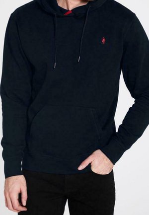 Man draagt een zwarte pullover hoodie met trekkoorden, een voorzak en een klein rood geborduurd logo op de borst.