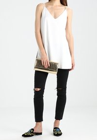 Biała bezrękawnikowa bluzka z dekoltem w serek, czarne poszarpane dżinsy, czarne wsuwane buty z kwiatową haftem oraz metaliczna złota kopertówka.