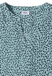 Chemise bleu clair avec motif carré irrégulier noir, col en V et étiquette de marque "Cecil" cousue à l'intérieur de l'encolure.