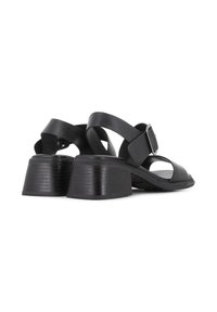 Sandalias de cuero negro con tacón grueso, que cuentan con tiras cruzadas y un hebilla lateral. Los tacones tienen una textura acanalada.