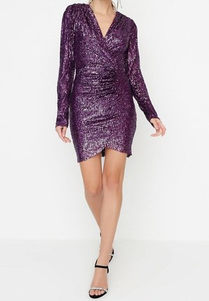 Robe violette à sequins avec manches longues, décolleté en V profond, silhouette ajustée et fente haute sur la cuisse. Texture lisse avec des accents réfléchissants.