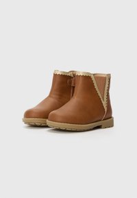 Bottes ankle en cuir marron avec des accents dorés festonnés, texture lisse, bout rond et semelle en caoutchouc contrastante.