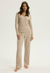 Beżowy zestaw odzieży domowej składający się z long-sleeve henley i dopasowanych spodni. Miękka tekstura, luźny krój i minimalne detale.