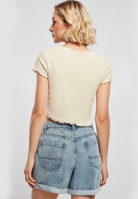 Beige, cropped póló, íves szegéllyel és rövid ujjakkal, világoskék farmer sorttal kombinálva, felcsatolt szegéllyel és hátsó zsebekkel.