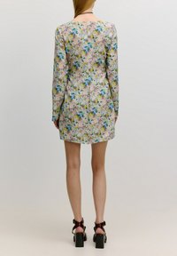 Bloemige jurk met lange mouwen, met een pastelachtergrond en blauwe, roze en gele bloemen; heeft een achternaad en een rechte zoom.