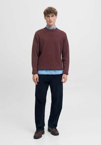 Maglione borgogna a trama sopra una camicia di jeans azzurra, abbinato a pantaloni in velluto a coste scuri e scarpe marroni, presentato su uno sfondo bianco.