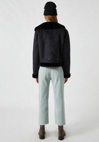 Černá kožichová bunda s límcem z umělé kožešiny, spárovaná se světle zelenými zkrácenými džíny a hnědými kotníkovými botami. Minimalistický design s čistými liniemi.