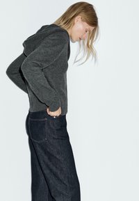 Felpa con cappuccio grigia in maglia, dal fit rilassato, abbinata a jeans in denim scuro. Design semplice, senza motivi visibili o dettagli in metallo.