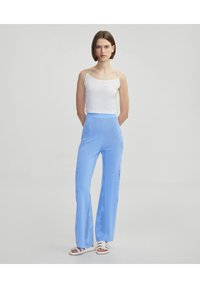 Lichtblauwe flared broeken met een textuurpatroon, gecombineerd met een witte camisole. De stof lijkt glad met een lichte glans.