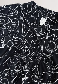 Czarny komplet piżamy z białym wzorem zwierząt i motywami niebieskimi, wykonany z miękkiej tkaniny. Zawiera bluzkę z kołnierzykiem i spodnie z elastyczną talią.