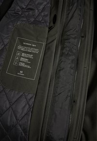 Intérieur d'une veste noire matelassée avec une étiquette d'informations techniques soulignant l'imperméabilité, la respirabilité et l'élasticité par Matinique.