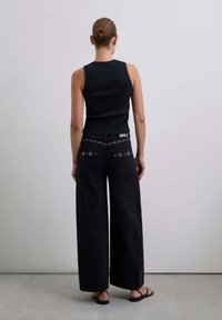 Top nero a costine abbinato a jeans di denim neri a gamba larga, con cuciture decorative sulla vita e sandali piatti.