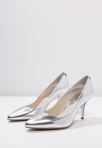 Talons aiguille en métal argenté avec un design à bout pointu, une texture lisse, une silhouette élégante et un talon stiletto.