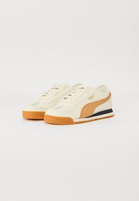 Sneaker crema con accenti arancioni e una striscia nera. Presentano una suola in gomma testurizzata e un classico design con lacci.