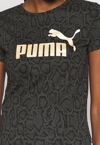 Czarny dopasowany t-shirt z teksturowanym nadrukiem wężowej skóry. Z przodu duże złote logo "PUMA" oraz sylwetka skaczącego pumy nad nim.