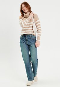 Jersey a rayas en beige y blanco con cuello alto, combinado con jeans rectos azules y zapatos color crema. Lleva un bolso blanco.