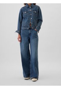 Chaqueta de denim con collar clásico, bolsillos frontales y cierre de botones, combinada con jeans de pierna ancha en un lavado azul medio y dobladillo deshilachado.