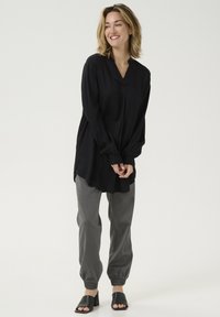Blusa negra de textura con mangas largas y escote en V, combinada con pantalones grises ajustados y sandalias de tacón negras. Diseño simple y moderno.