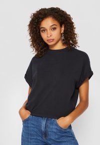 Schwarzes Baumwoll-T-Shirt mit kurzen Ärmeln, aufgerollten Bündchen und Rundhalsausschnitt, kombiniert mit blauen Jeans. Einfaches, lässiges Design.