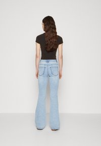 Lyseblå flared jeans med høy livhøyde, som har to baklommer og en subtil falmet tekstur. Kombinert med en tettsittende svart topp.