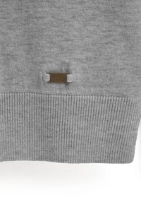 Grauer Pullover mit glatter Strickstruktur, mit einem gerippten Saum und einem kleinen Bronzeschild, auf dem "POLO CLUB" steht.
