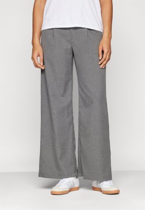 Lichtgrijze wijde broek met voorplooien, gemaakt van textuurstof, gecombineerd met witte schoenen en een kort wit shirt.