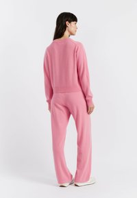 Pullover rosa a maglia con scollatura rotonda e polsini a coste, abbinato a pantaloni ampi coordinati, che mettono in mostra una consistenza morbida.