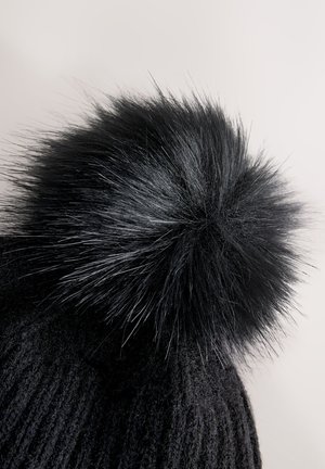 Cappellino nero lavorato a maglia con un grande pompon nero soffice sulla parte superiore, con un motivo a coste testurizzato su tutto il corpo del cappello.