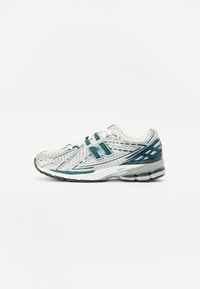 Hvit sportsko med teal detaljer, mesh-overdel, gummisåle og forsterket tåhette. Har en fremtredende 'N'-logo på siden.