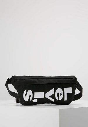 Sac banane en tissu noir avec des lettres blanches en gras épelant partiellement "Levi's" à l'avant, présenté sur une surface blanche.