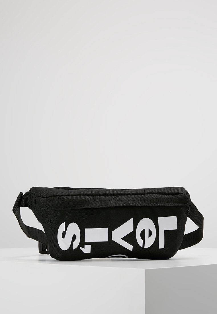 Sac banane en tissu noir avec des lettres blanches en gras épelant partiellement "Levi's" à l'avant, présenté sur une surface blanche.