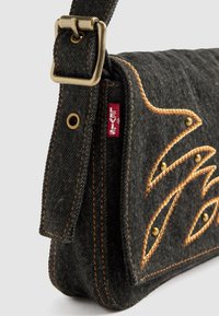 Sacoche en denim noir avec des coutures orange, des clous décoratifs en métal et une boucle en bronze. Présente une étiquette logo Levi's sur le côté.
