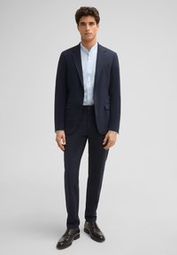 Marineblauw pak met een slim fit, colbert met één knoop en bijpassende broeken. Draag het met een lichtblauw shirt en donkere leren schoenen. Soepele stoftextuur.