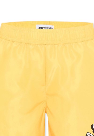 Pantalones cortos con cintura elástica amarilla, etiqueta Moschino y gráfico parcial en blanco y negro en la parte inferior derecha de la pierna.