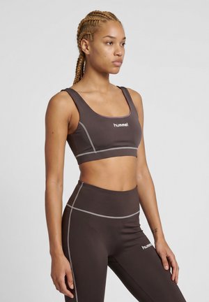 Kvinde med flettet hår iført en mørk sports-bh og højtaljede leggings med hvide syninger, begge mærket med "hummel" logo.