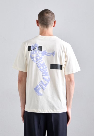 Cremfarbendes Baumwoll-T-Shirt mit einem großen lila Grafikdesign und schwarzen rechteckigen Akzenten auf der Rückseite. Kurze Ärmel und lockere Passform.