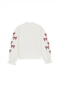 Balta garām piedurknēm topiņš ar pūkainām piedurknēm, kuram ir sarkani izšūti samta loku motīvi gar ārējām rokām. Tekstūrēta adīta apkakle un elastīgas aproces.